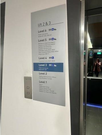 Photograph of Braille signage outside lift which is very extensive, however due to the amount of information and the formatting of the sign, is not height friendly for hands to read Braille